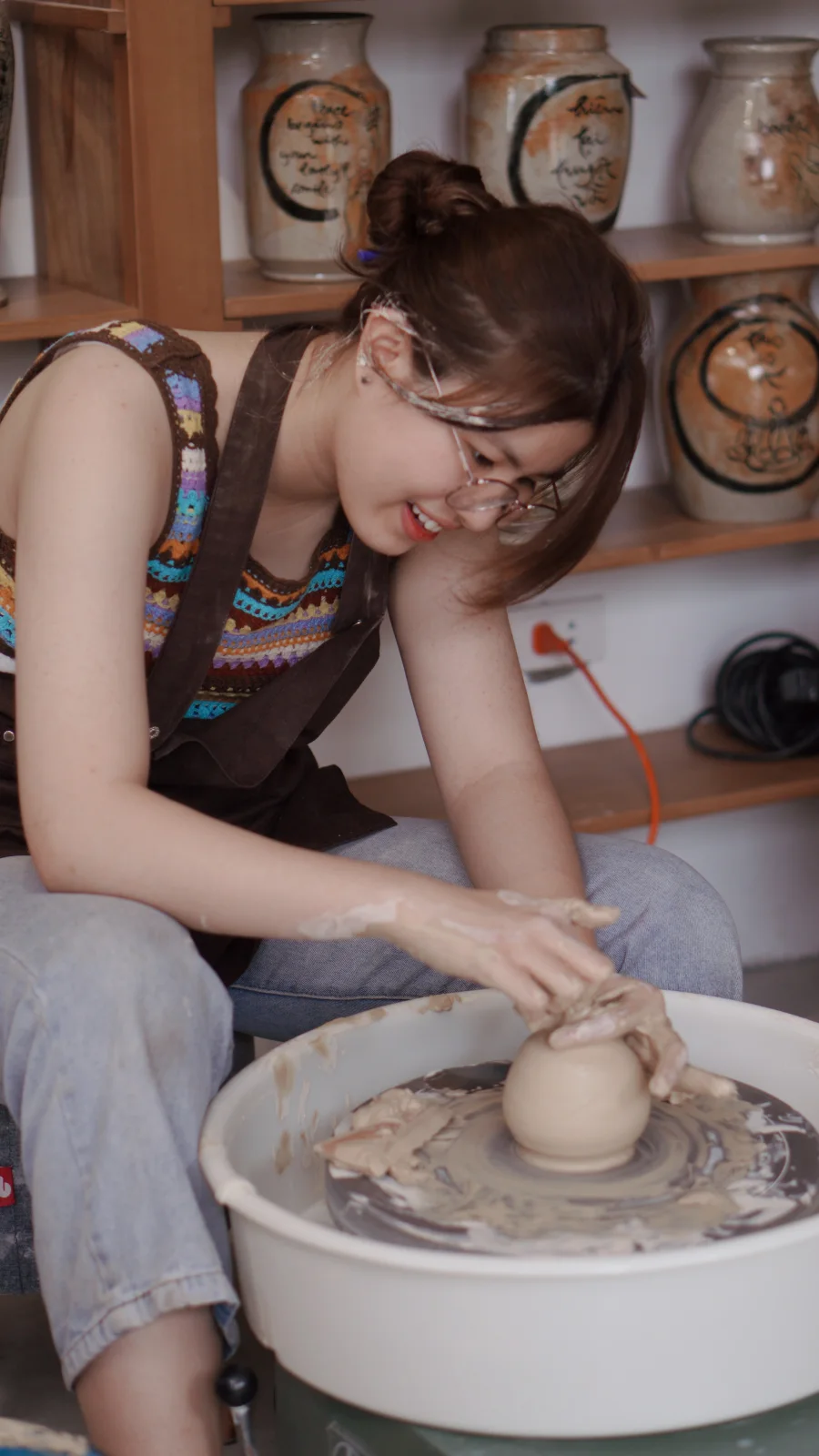 A student forming clay on the pottery wheel